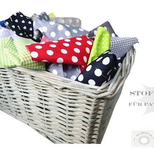 Könnte beinhalten: Ein weißer Weidenkorb gefüllt mit bunten Stoffquadraten. Die Stoffquadrate haben Punkte, Karomuster und Sterne. Der Korb ist mit "Stoffpaket für Patchwork" und "Stoffe und-Co." beschriftet.