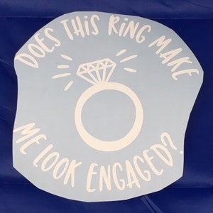 May include: White vinyl sticker with the text "Does this ring make me look engaged?" and a stylized diamond ring with a sparkle effect.