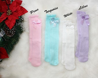 May include: Knee-high socks in pink, turquoise, white, and lilac, each with a bow at the top. The socks have a ribbed texture and a ruffled edge. The word "Pine", "Turquoise", "White", and "Lilac" are written above each pair of socks.