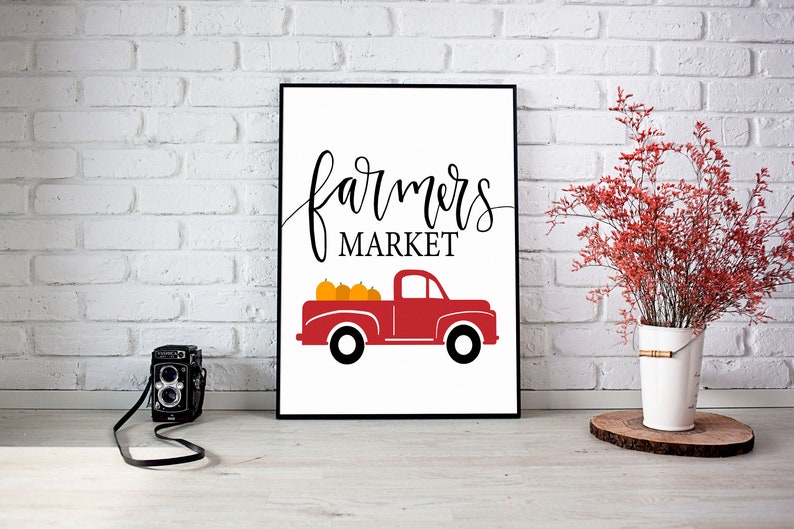 May include: A white sign with black text that reads "farmers market" and a red pickup truck with orange pumpkins in the bed.