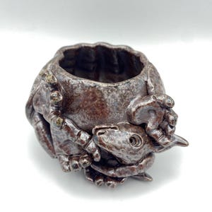 May include: A small, brown ceramic planter shaped like a curled-up animal with a textured surface. The planter has a round opening at the top for planting.