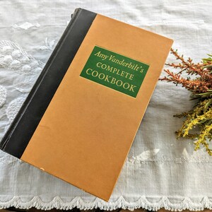 May include: A vintage hardcover cookbook titled "Amy Vanderbilt's Complete Cookbook" with a green spine and orange cover.