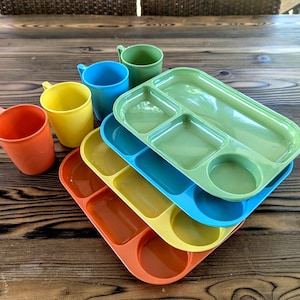 May include: A collection of colorful, vintage-style plastic trays and cups. The trays are divided into compartments and come in orange, yellow, blue, and green. The cups are orange, yellow, blue, and green. A nostalgic set for picnics or meals.