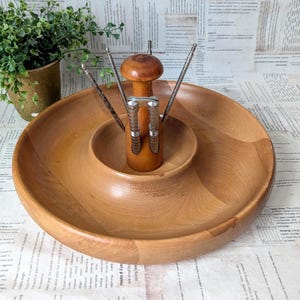 May include: A vintage wooden serving tray with a built-in nutcracker and picks. The tray is light brown and has a circular design with a raised center. The nutcracker is made of wood and metal.