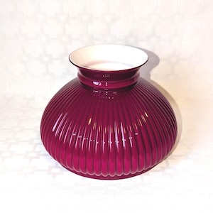 May include: A deep burgundy glass lampshade with a ribbed exterior and a white interior. The lampshade has a rounded, bulbous shape with a flared top. The ribbed design creates a textured surface, and the white interior reflects light.