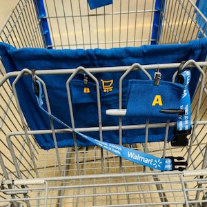 May include: A metal shopping cart featuring a blue fabric liner with yellow letters A, B, and C attached by metal clips. A blue Walmart branded seat belt strap is attached to the cart frame. A white marker is tucked into the fabric label marked A.