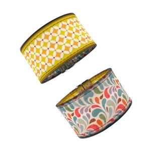 Könnte beinhalten: Zwei Stoff-Armbänder mit unterschiedlichen Mustern. Ein Armband hat einen gelben Hintergrund mit einem weißen und orangefarbenen geometrischen Muster. Das andere Armband hat einen cremefarbenen Hintergrund mit einem bunten Blumenmuster.
