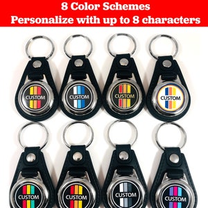 May include: Eight black leather keychains with silver metal rings and round metal tags. Each tag has a different color scheme of four stripes with the word "CUSTOM" printed in white.