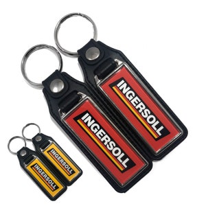 Può includere: Una collezione di portachiavi con la scritta "INGERSOLL" in bianco su sfondo rosso, con strisce gialle e nere. I portachiavi hanno un retro in pelle nera e un portachiavi argentato.