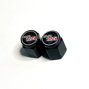 May include: Two black valve stem caps with the text "TRAIL 125" in white and red. The caps have a hexagonal shape and a glossy finish. The text is in a circular design.