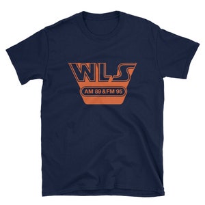 Op de afbeelding: Een marineblauw t-shirt met een oranje afbeelding van het WLS-radiostationlogo. Het logo toont de tekst "WLS" in een retro-lettertype met de tekst "AM 89 & FM 95" eronder.