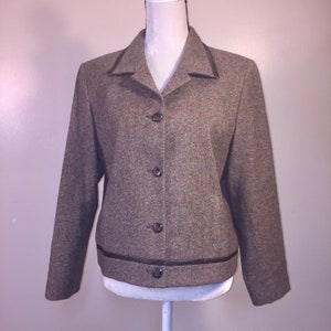Op de afbeelding: Een bruine tweed blazer met een bruine leren bies rond de kraag en de zoom. De blazer heeft vier knopen aan de voorkant.
