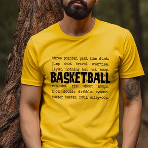 May include: Yellow t-shirt with black text that reads "three pointer. pass. slam dunk. jump shot. travel. overtime. layup. nothing but net. hoop. BASKETBALL rebound. rim. shoot hoops. shot. double dribble. swoosh. buzzer beater. foul. alley-oop."