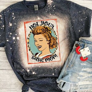 May include: A dark blue t-shirt with a bleached design featuring a vintage illustration of a woman winking with the text "not your basic mom".