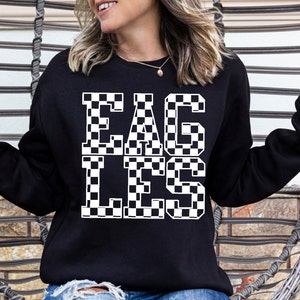 May include: Black sweatshirt with the word "EAGLES" in large, white, checkered letters. The sweatshirt is a crew neck style and is being worn by a person.
