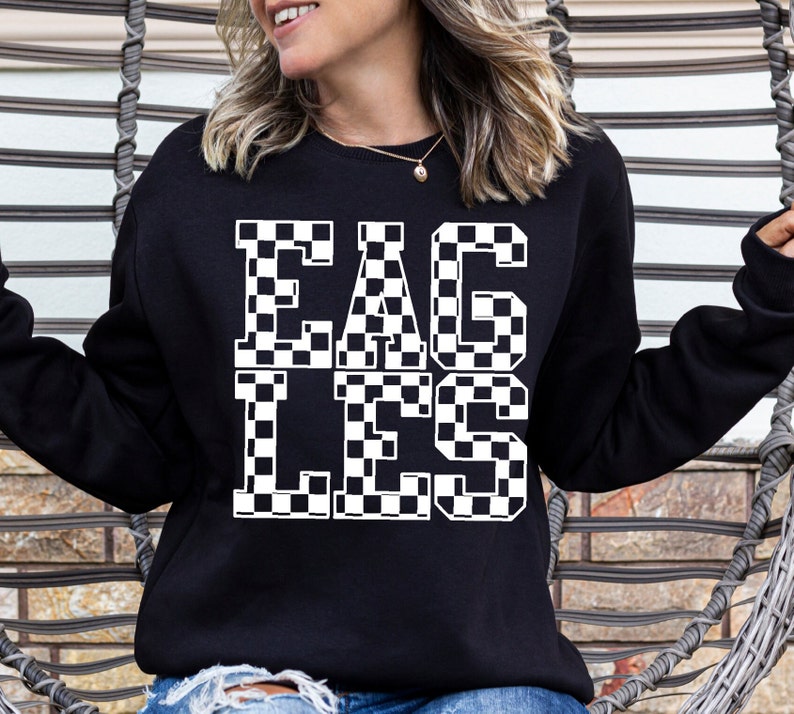 May include: Black sweatshirt with the word "EAGLES" in large, white, checkered letters. The sweatshirt is a crew neck style and is being worn by a person.