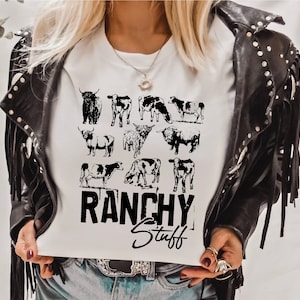 May include: White t-shirt with a black and white graphic of cows and the text "Ranchy Stuff".