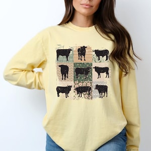 May include: A yellow long-sleeved shirt with a patchwork design featuring black silhouettes of cows. The patchwork design includes floral and geometric patterns in shades of green, brown, and pink.