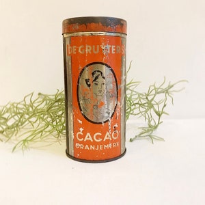Pode incluir: Lata vintage laranja e prata com o texto "De Gruyters Cacao Oranjemerk" e uma ilustração em preto e branco de um rosto de mulher.
