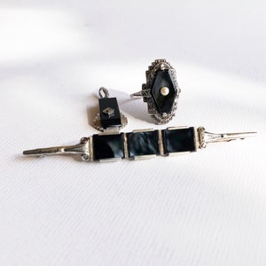 May include: A set of three vintage jewelry pieces featuring black onyx and silver. The set includes a ring, a brooch, and a pair of earrings.