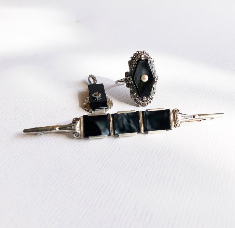 May include: A set of three vintage jewelry pieces featuring black onyx and silver. The set includes a ring, a brooch, and a pair of earrings.