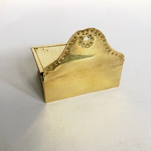 Pode incluir: Um pequeno porta-palitos de f&oacute;sforo de lat&atilde;o com uma parte superior decorativa festoneada. O porta-palitos tem uma tampa com dobradi&ccedil;as e uma base retangular.