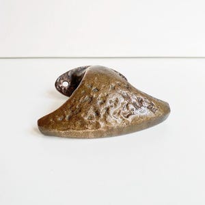 May include: A bronze-toned, textured metal door handle with an oval backplate and a curved, organic form. The handle has a rough, uneven surface and a small hole in the backplate for mounting. The design suggests a vintage or rustic style.