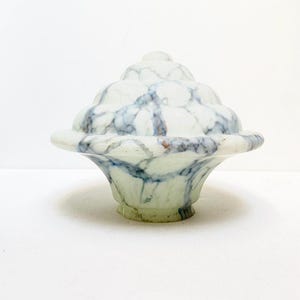 Könnte beinhalten: Ein weißer Glaslampenschirm mit einem Marmormuster in Blautönen und Braun. Der Lampenschirm hat eine abgerundete Oberseite und eine breite, flache Basis.