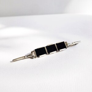 May include: A silver brooch with three black square stones set in a row. The brooch has a simple, elegant design.