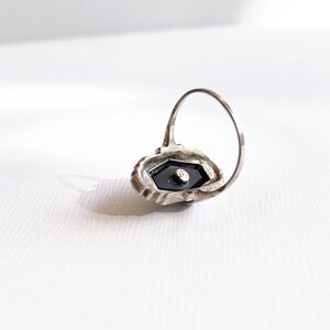 May include: A silver ring with a black stone set in a hexagonal shape. The ring is detailed with intricate silverwork.