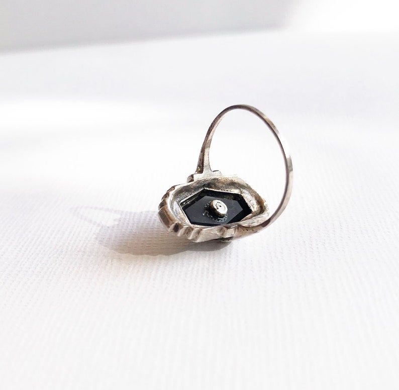 May include: A silver ring with a black stone set in a hexagonal shape. The ring is detailed with intricate silverwork.