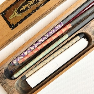 May include: A wooden box with a decorative lid containing four pencils with patterned paper wrapped around them and a white eraser.