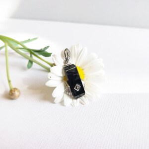 May include: A black gemstone pendant with a silver setting and a small diamond accent. The pendant is resting on a white daisy.