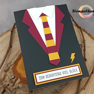 Könnte beinhalten: Eine schwarze Karte mit einem roten und goldenen Anzug- und Krawatten-Design. Die Karte trägt den Text "Zum Geburtstag viel Glück" auf einem gelben Banner.