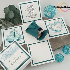 Könnte beinhalten: Eine handgefertigte Geschenkbox in Türkis und Weiß mit verschiedenen dekorativen Elementen. Die Box enthält bedruckte Karten mit Segelboot- und Taubenillustrationen sowie deutschen Text. Dekorative türkisfarbene Drahtkugeln und ein türkisfarbener Papiergeldhalter sind ebenfalls vorhanden.