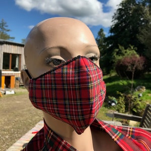 May include: A red and black tartan face mask with a black elastic band. The mask is made of fabric and has a sewn-in seam around the edges.