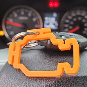 May include: An orange car key chain shaped like a check engine light symbol. The keychain is attached to a silver key ring and a black car key.