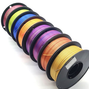 May include: A set of seven spools of filament for 3D printing. The spools are arranged in a stack, with the colours of the filament progressing from red to gold. The spools are all black and have a label on the side.
