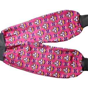 Könnte beinhalten: Rosa und graue Stoffhose mit einem geometrischen Muster aus gelben, weißen und blauen Blumen. Die Hose hat elastische Bündchen an den Knöcheln.