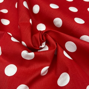 May include: Close-up of a red fabric with large white polka dots. The fabric is gathered in a swirl, showing the texture and folds of the material. The bright red color and contrasting white dots create a classic, playful pattern.
