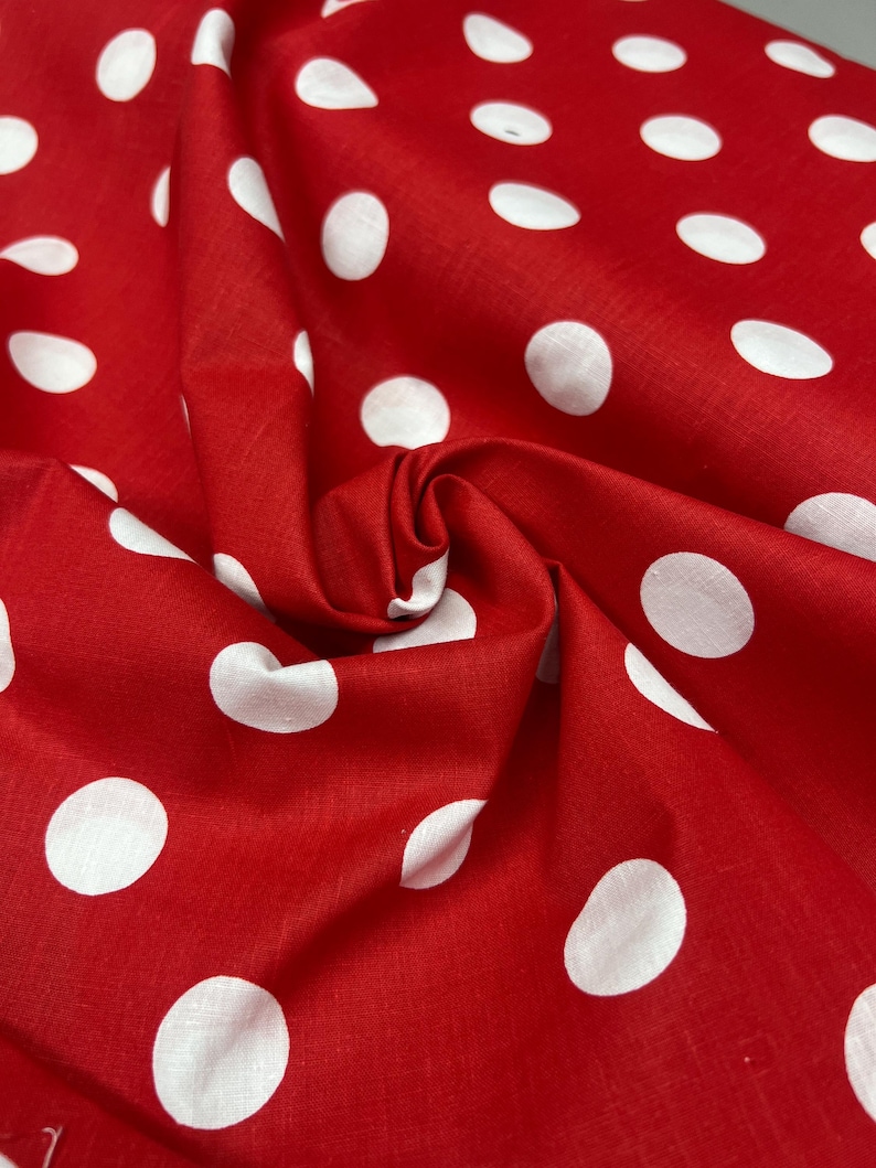 Puede incluir: Primer plano de una tela roja con grandes lunares blancos. La tela est&aacute; arrugada, revelando su textura y pliegues. El rojo brillante y los lunares blancos crean un patr&oacute;n cl&aacute;sico y alegre, ideal para diversos proyectos de manualidades.