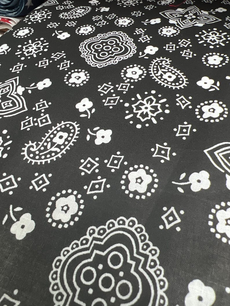 May include: Black fabric with a white paisley pattern. The pattern includes paisley shapes, diamonds, and small flowers.