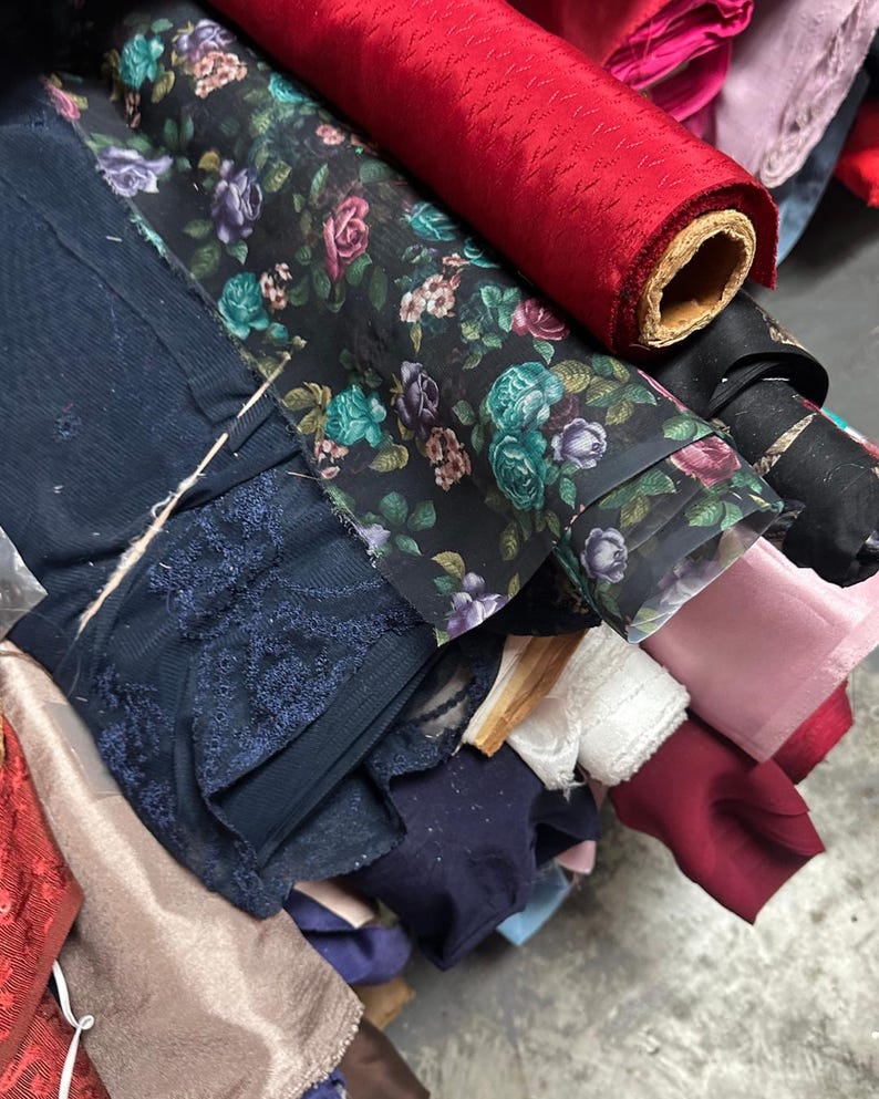 Puede incluir: Una variedad de rollos de tela en diferentes colores y patrones, incluyendo florales, de encaje y colores s&oacute;lidos. Los rollos est&aacute;n apilados uno encima del otro, creando una exhibici&oacute;n colorida y texturizada.