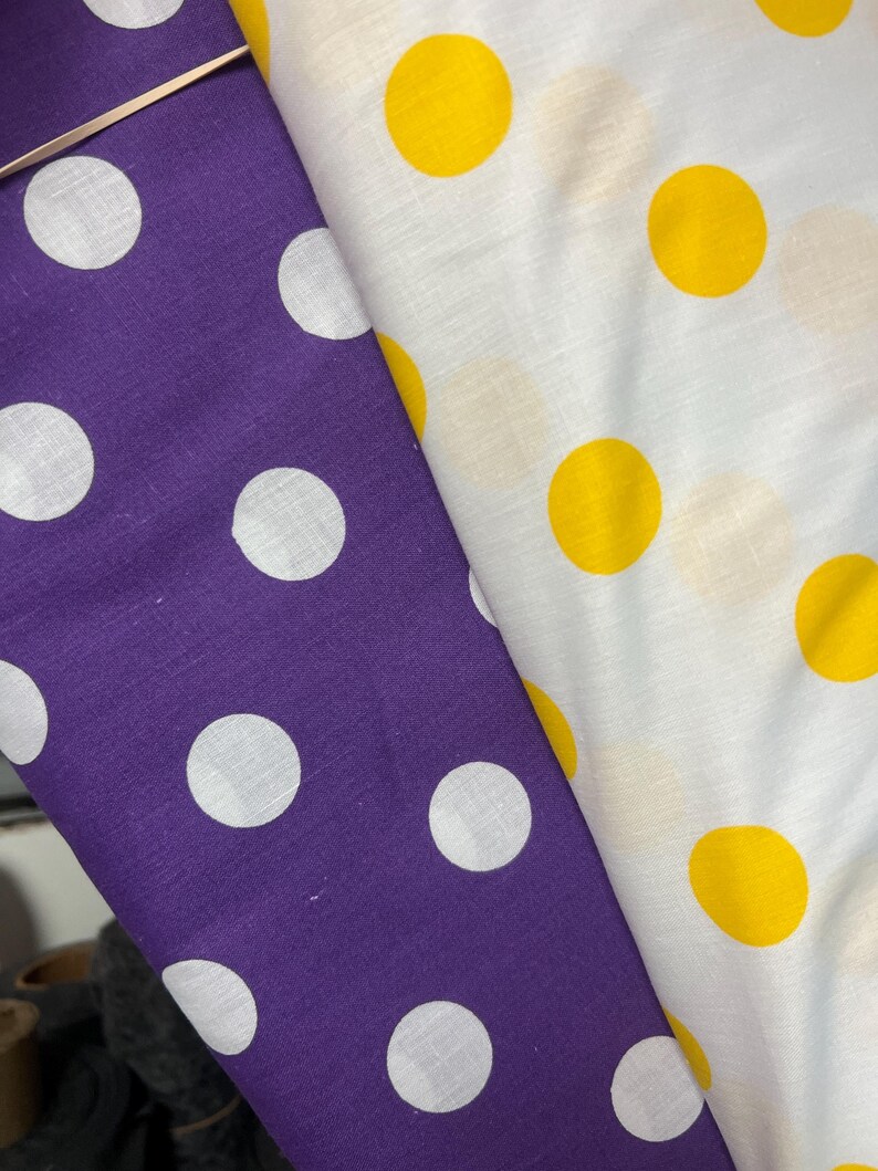 Puede incluir: Dos telas con estampado de lunares. Una es morada con lunares blancos, la otra blanca con lunares amarillos. Las telas est&aacute;n dobladas una sobre otra, mostrando los diferentes patrones y colores.