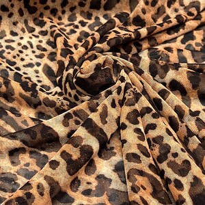 K&ouml;nnte beinhalten: Nahaufnahme eines Stoffes mit Leopardenmuster. Der Stoff hat einen beigefarbenen Hintergrund mit dunkelbraunen Flecken und Markierungen, wodurch ein wildes Tiermuster entsteht. Der Stoff ist gefaltet und zeigt die Textur und das Muster.