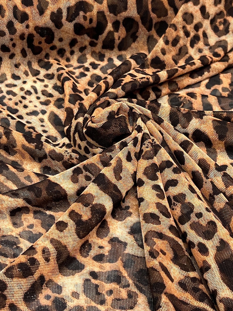 K&ouml;nnte beinhalten: Nahaufnahme eines Stoffes mit Leopardenmuster. Der Stoff hat einen beigefarbenen Hintergrund mit dunkelbraunen Flecken und Markierungen, wodurch ein wildes Tiermuster entsteht. Der Stoff ist gefaltet und zeigt die Textur und das Muster.