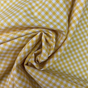 May include: Close-up of yellow and white gingham fabric. The fabric is folded and draped, showing the texture and pattern. The pattern is a classic checkered design, with squares of yellow and white.