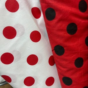 Puede incluir: Dos telas con estampados de lunares. Una es blanca con grandes lunares rojos, la otra es roja con grandes lunares negros. Las telas est&aacute;n dobladas, mostrando el patr&oacute;n y la textura del material. La imagen est&aacute; bien iluminada, resaltando los colores.