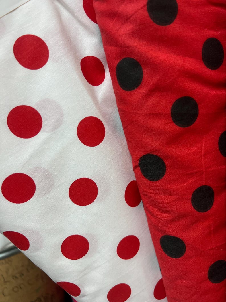 Puede incluir: Dos telas con estampados de lunares. Una es blanca con grandes lunares rojos, la otra es roja con grandes lunares negros. Las telas est&aacute;n dobladas, mostrando el patr&oacute;n y la textura del material. La imagen est&aacute; bien iluminada, resaltando los colores.