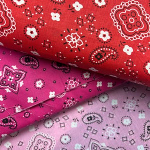 May include: Three pieces of fabric with a paisley bandana print. The top fabric is red with white and black paisley designs. The middle fabric is pink with white and black paisley designs. The bottom fabric is light pink with white and black paisley designs.